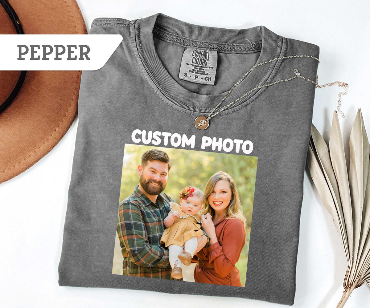 May include: A pepper-colored short-sleeve t-shirt featuring a custom photo print of a family of three, including a man, a woman, and a baby. The shirt has a Comfort Colors brand label at the neck and the text CUSTOM PHO