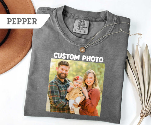 May include: A pepper-colored short-sleeve t-shirt featuring a custom photo print of a family of three, including a man, a woman, and a baby. The shirt has a Comfort Colors brand label at the neck and the text CUSTOM PHO