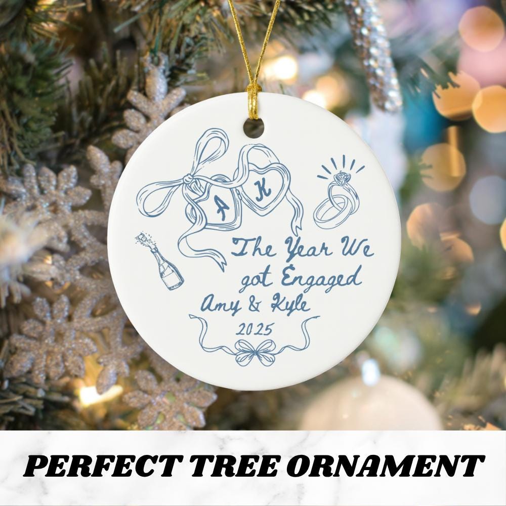 May include: White ceramic Christmas tree ornament with a gold string for hanging. The ornament features blue line art of engagement rings, champagne, and ribbons. Text reads "The Year We got Engaged Amy &amp; Kyle 