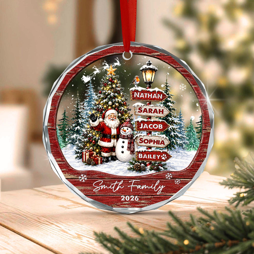 May include: A round Christmas ornament featuring a festive winter scene with Santa Claus and a snowman standing near a decorated tree. A signpost displays the names Nathan, Sarah, Jacob, Sophia, and Bailey. The text Smi