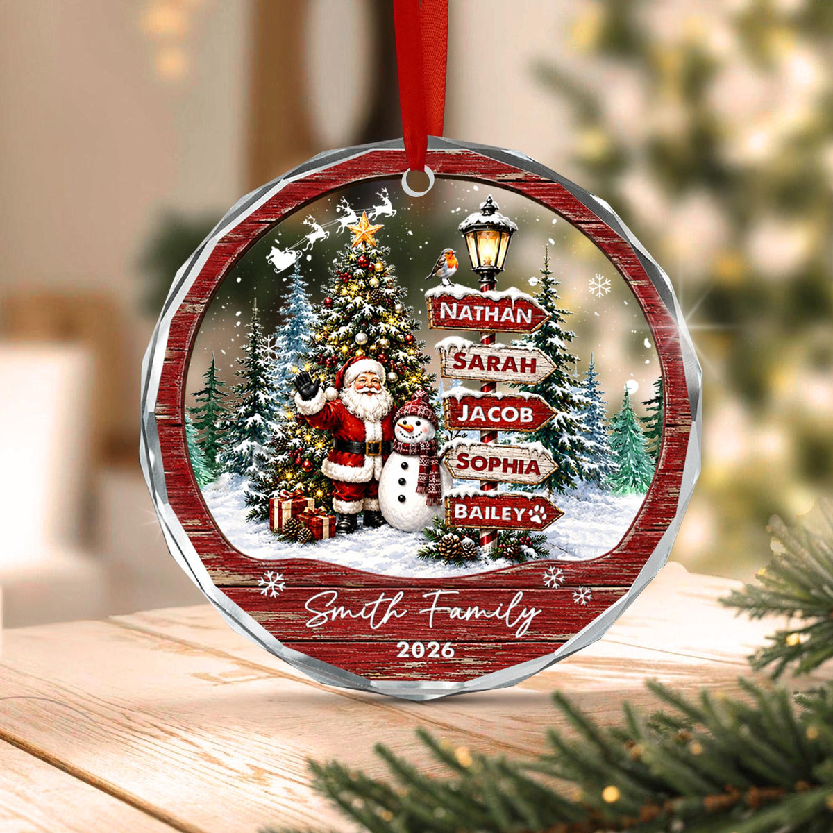 May include: A round Christmas ornament featuring a festive winter scene with Santa Claus and a snowman standing near a decorated tree. A signpost displays the names Nathan, Sarah, Jacob, Sophia, and Bailey. The text Smi