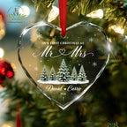 May include: A heart-shaped clear glass ornament with faceted edges, hanging from a red ribbon. It features the text "OUR FIRST CHRISTMAS AS Mr &amp; Mrs", "David &amp; Carrie", and "2026" a