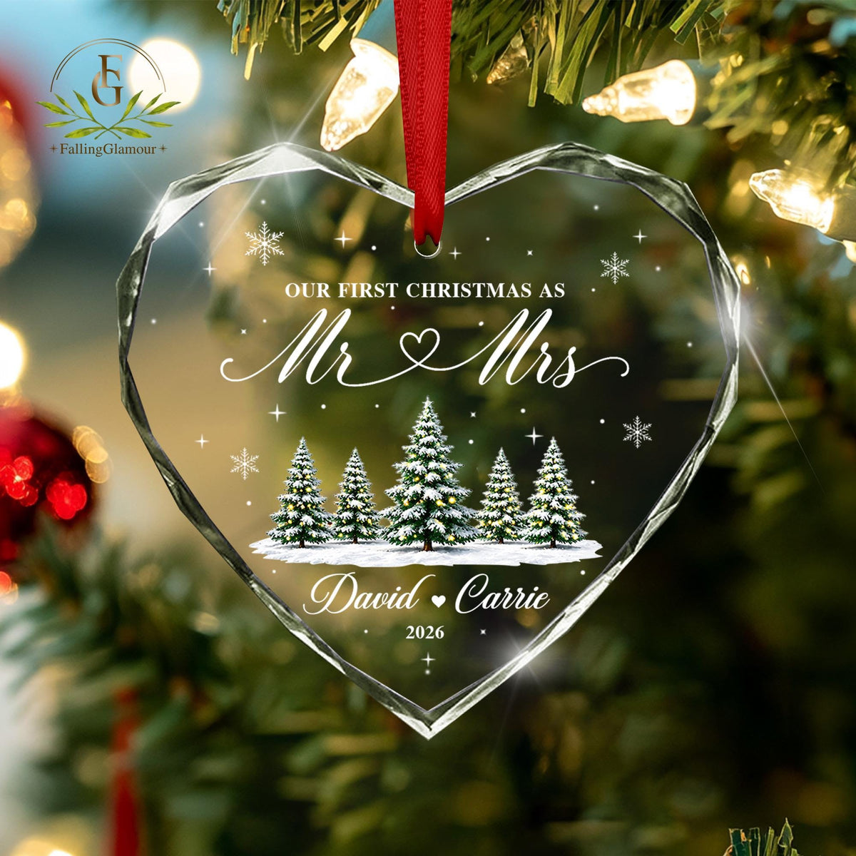 May include: A heart-shaped clear glass ornament with faceted edges, hanging from a red ribbon. It features the text "OUR FIRST CHRISTMAS AS Mr &amp; Mrs", "David &amp; Carrie", and "2026" a