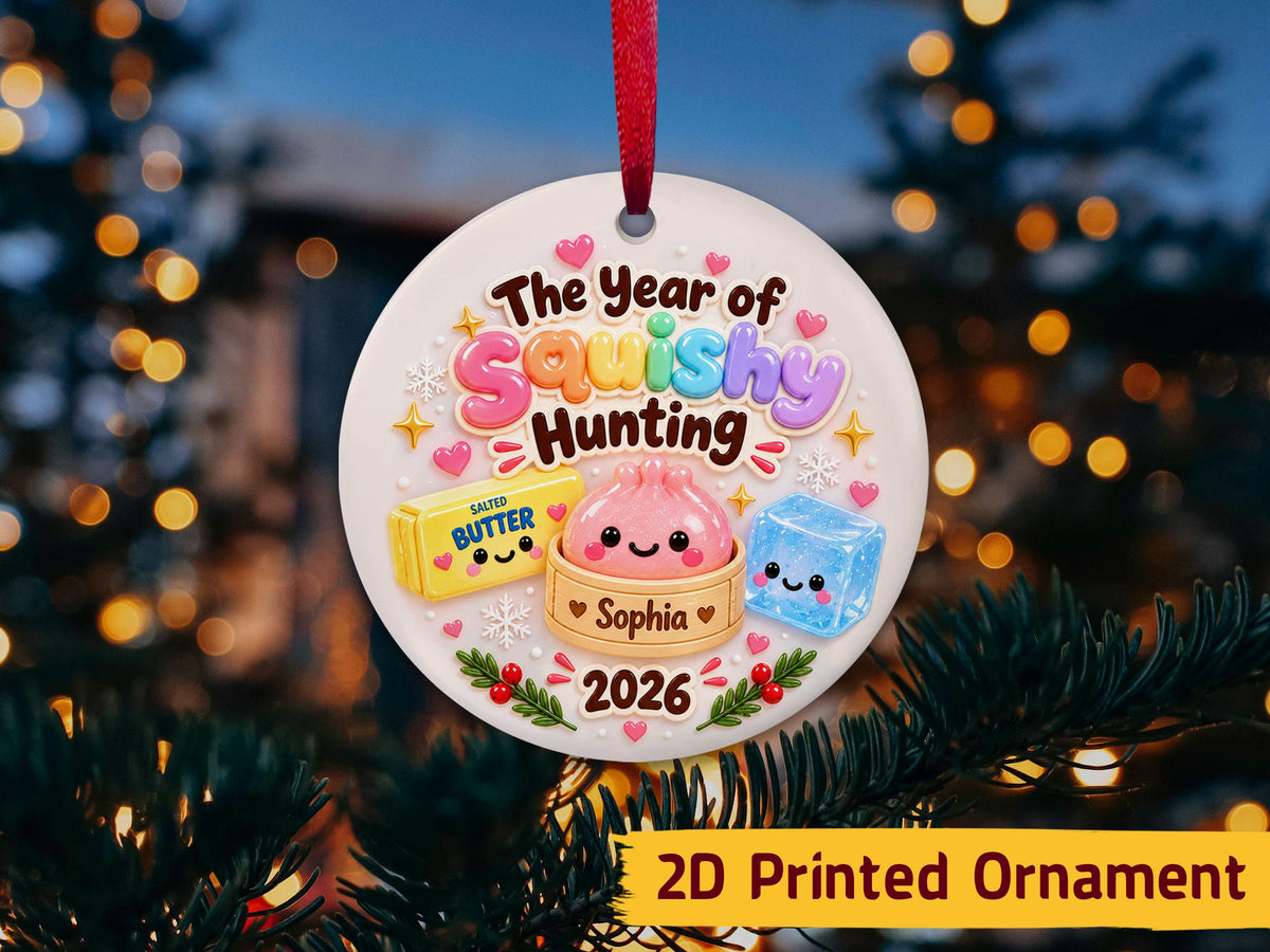 May include: A round white ceramic ornament with a red ribbon featuring the text The Year of Squishy Hunting and 2026. The design includes a cartoon stick of salted butter, a pink dumpling in a bamboo steamer labeled Sop