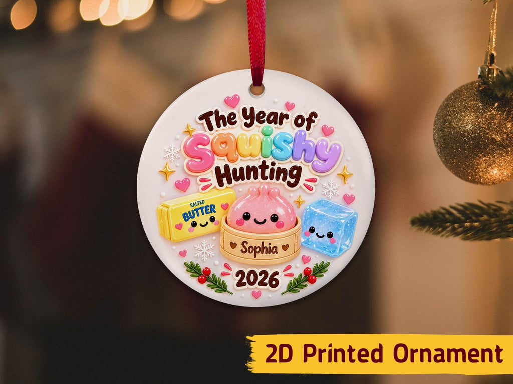 May include: A round white ceramic ornament with a red ribbon featuring the text The Year of Squishy Hunting, a yellow butter stick, a pink dumpling in a steamer basket labeled Sophia, a blue ice cube, small hearts, snow