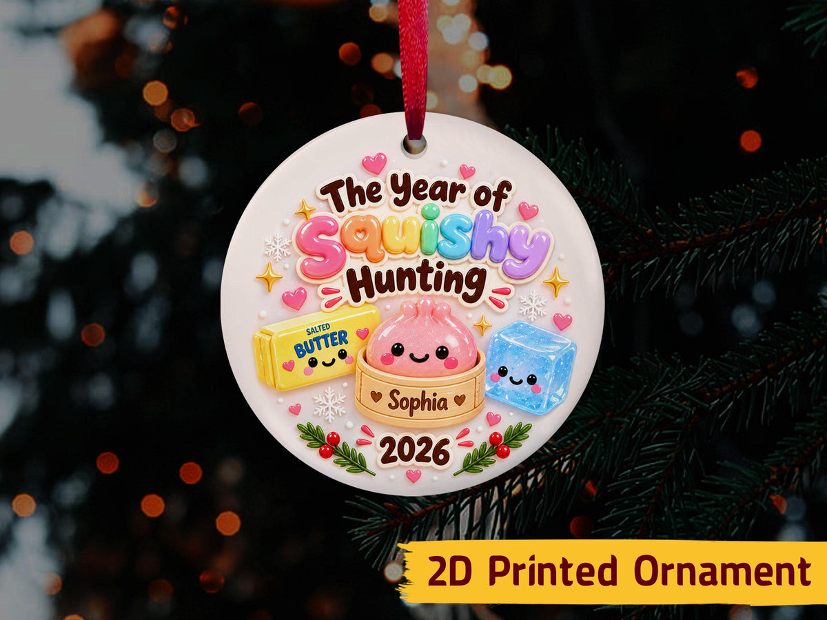 May include: A round white ceramic ornament hanging from a red ribbon. It features the text The Year of Squishy Hunting, a yellow stick of salted butter, a pink dumpling in a bamboo steamer labeled Sophia, a blue ice cub